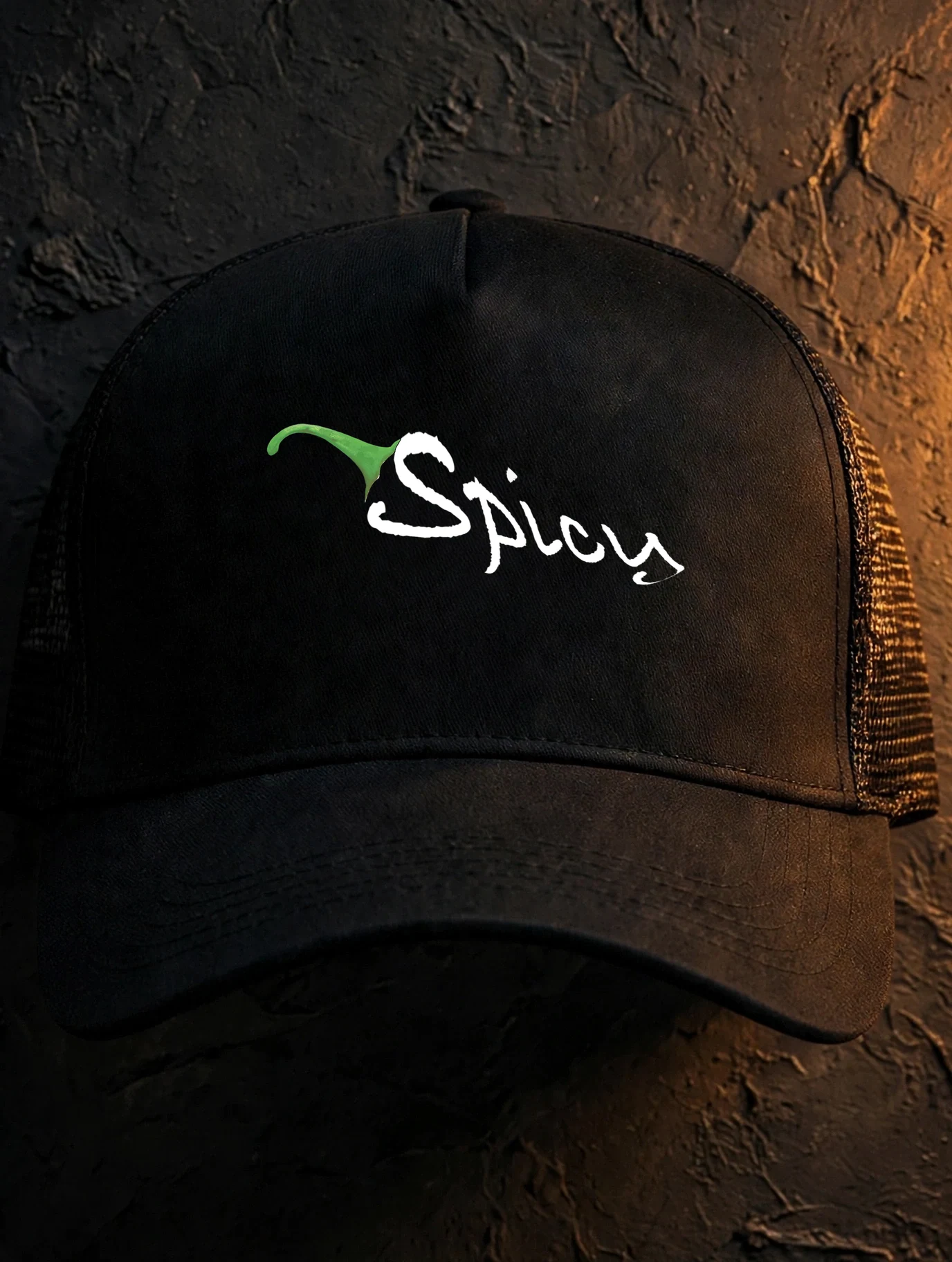 Black trucker cap with the Spicy script embroidered in white on the front panel, dark studio